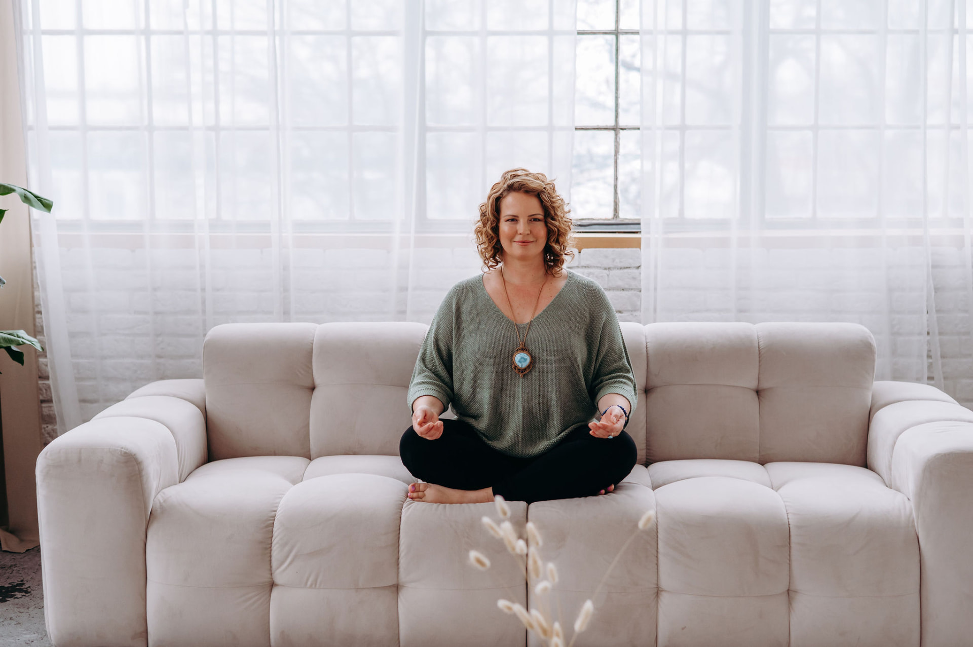 Petra Zlotá seated in meditation on a light sofa before a bright window