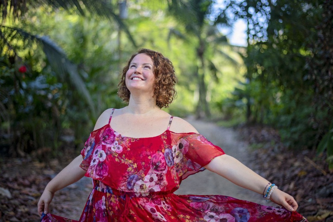 Petra Zlotá laughing on a forest path, arms open, in a red floral dress