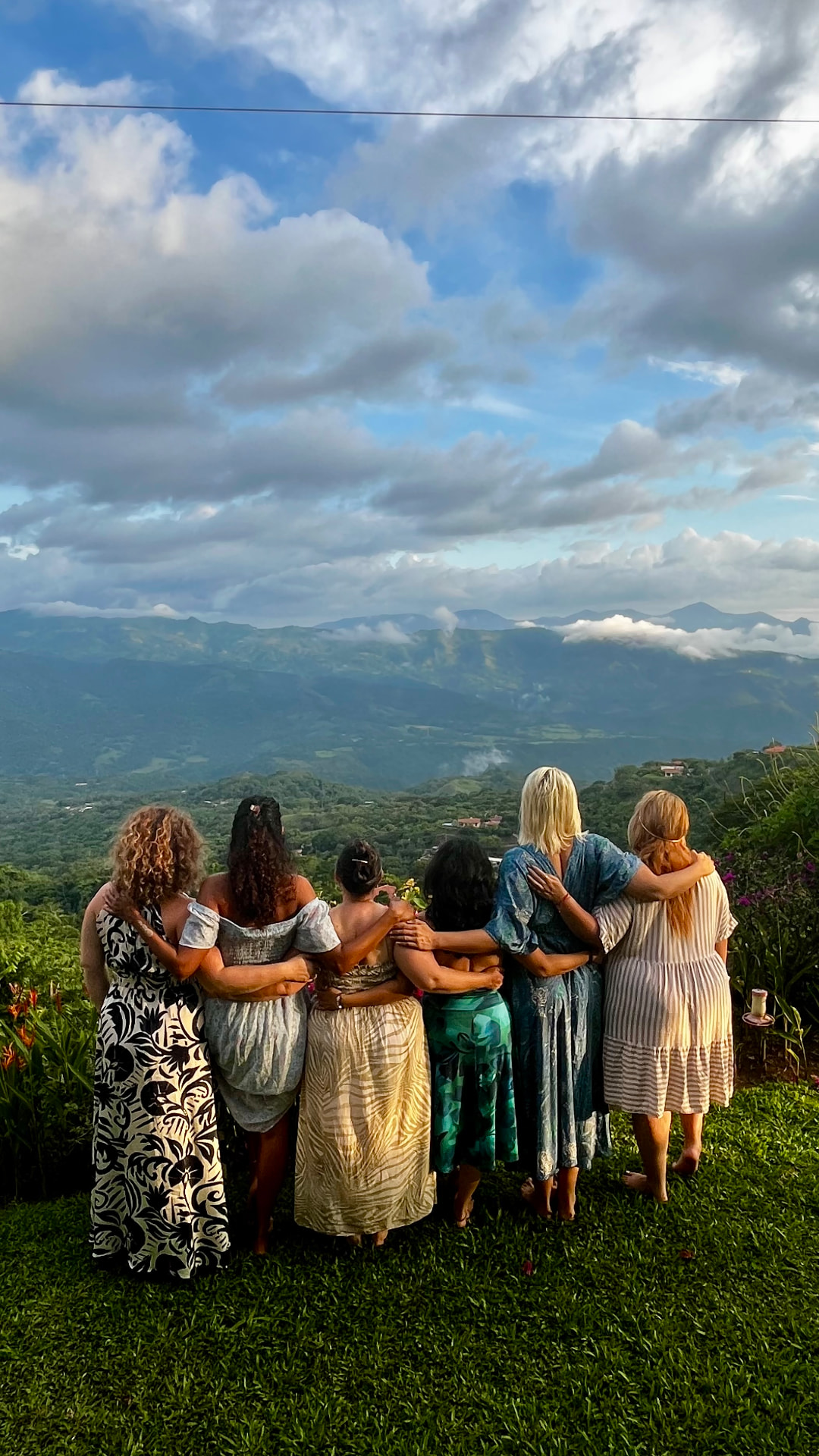 A group of women, arms around each other, overlooking green mountains